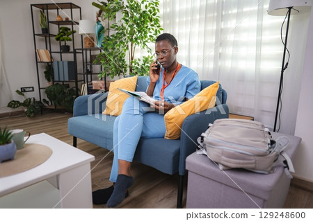 Young female doctor talking on the phone and reading notes at home 129248600
