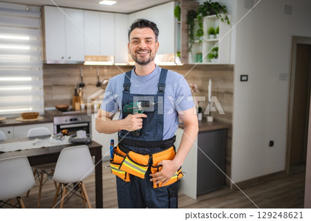 Handyman smiling and holding cordless drill in kitchen 129248621