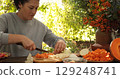 Woman prepares delicious Thanksgiving feast outdoors, chopping fresh vegetables in serene garden setting, showcasing commitment to holiday traditions and family gatherings 129248741