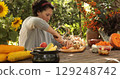 Woman skillfully prepares Thanksgiving feast outdoors, immersed in vibrant fall atmosphere filled with fresh ingredients and colorful decorations, capturing essence of seasonal celebration and warmth 129248742