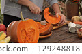 Pumpkin preparation process captures essence of autumn festivities at rustic outdoor kitchen during harvest season, showcasing hands skillfully cutting ripe pumpkin with sharp knife for cooking 129248818