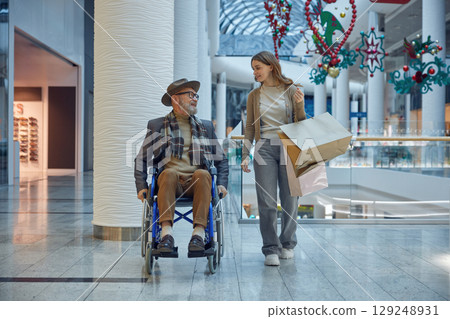 A man in a wheelchair is assisted by a woman in a mall A man in a wheelchair is assisted by a woman in a mall 129248931