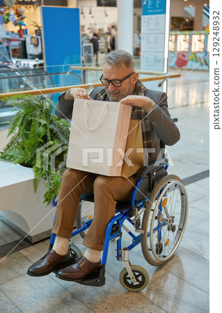 A man who is sitting in a wheelchair is holding a shopping bag while at a mall 129248932