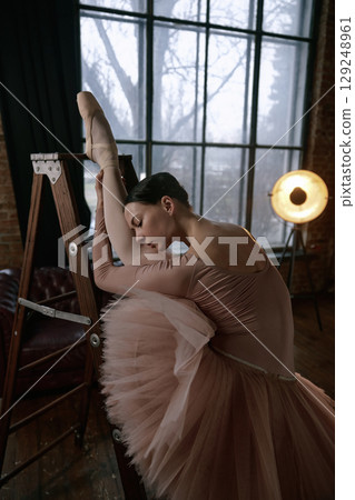 A ballet dancer performs on a ladder, showcasing her exquisite stretch and graceful artistry 129248961