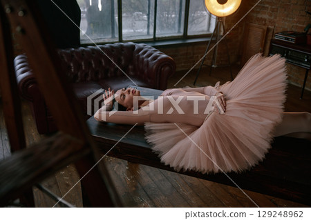 An elegant and graceful ballerina posed on a dark table surrounded by soft tutu fabric 129248962