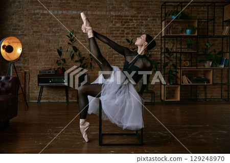 A graceful ballerina in a beautiful tutu practicing her moves in a serene studio setting 129248970