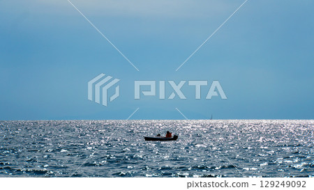 一艘小船和一個人的輪廓漂浮在海面上，陽光反射在水面上 129249092