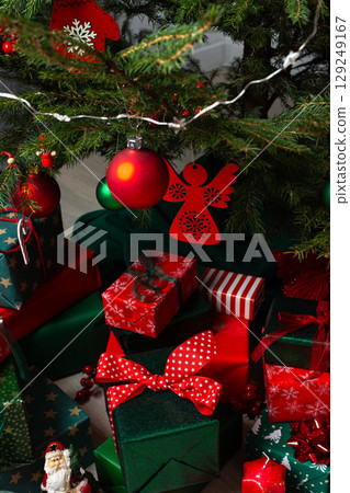 A festive display of green and red gift boxes under a beautifully decorated Christmas tree, complemented by candles and traditional ornaments, evoking warmth and holiday cheer A festive display of green and red gift boxes under a beautifully decorated Christmas tree, complemented by candles and traditional ornaments, evoking warmth and holiday cheer 129249167