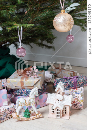 Vibrant pink and purple gift boxes with shiny ribbons rest under a Christmas tree adorned with glowing lights, creating a playful and joyful festive scene 129249170