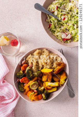 A nutritious breakfast showcases a bowl of quinoa accompanied by vibrant baked sweet potatoes, carrots, zucchini, beans, and turmeric chicken, paired with a fresh salad on the side 129249171