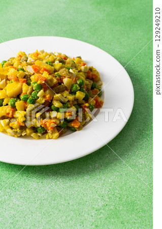A vibrant salad showcases a mix of boiled egg, tender chicken breast, diced potatoes, sweet carrots, and green peas, all drizzled with olive oil, perfect as a nutritious meal 129249210