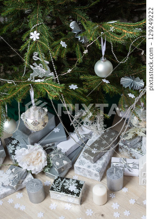 Modern and chic steel-tone gift boxes arranged beneath a beautifully decorated Christmas tree, complemented by candlelight and festive accents for a serene holiday mood Modern and chic steel-tone gift boxes arranged beneath a beautifully decorated Christmas tree, complemented by candlelight and festive accents for a serene holiday mood 129249222