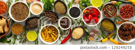 Assorted cooking spices and herbs arranged on a gray surface, featuring natural tones that add depth and aroma to any meal, banner 129249258