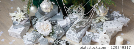 A cozy holiday scene featuring metallic steel-colored gift boxes, flickering candles, and intricate decorations under the Christmas tree, exuding warmth and seasonal cheer, banner 129249317
