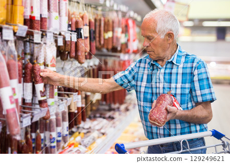 mature senor choosing uncooked smoked sausages in sausage department supermarket 129249621