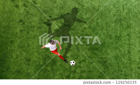 Contemporary collage of soccer player about to kick ball with exaggerated shadow cast across green field 129250135