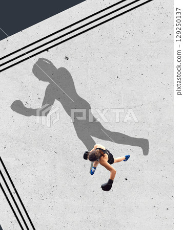 Collage of young female boxer in black gear casting oversized powerful shadow on light ring floor 129250137