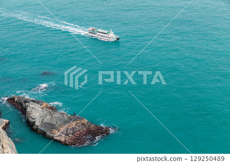 Aerial View of a Boat Sailing Near Rocky Coastal Waters 129250489