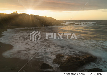 Sea waves crash against rocks at sunset, highlighting climate change impact on coastal ecosystems 129250920