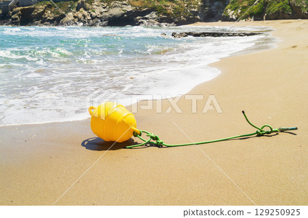 Yellow buoy washed ashore near the calm beach highlighting marine weather challenges 129250925