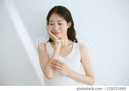 微笑的年輕女子觸摸她的皮膚並進行皮膚護理 — 自然光，白色背景 129251660