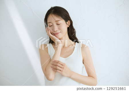 微笑的年輕女子觸摸她的皮膚並進行皮膚護理 — 自然光，白色背景 129251661