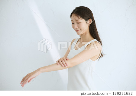 微笑的年輕女子觸摸她的皮膚並進行皮膚護理 — 自然光,白色背景 微笑的年輕女子觸摸她的皮膚並進行皮膚護理 — 自然光,白色背景 129251682