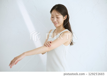 微笑的年輕女子觸摸她的皮膚並進行皮膚護理 — 自然光，白色背景 129251683