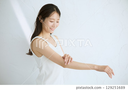 Smiling young woman touching her skin and doing skin care - Natural light, white background 129251689
