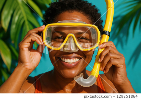 Smiling woman in yellow snorkeling mask poses outdoors with tropical leaves and blue background in bright sunlight, AI Generative 129251864