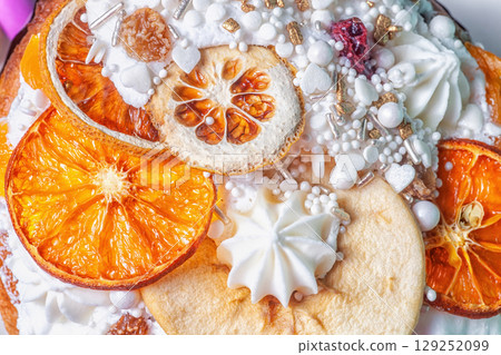 Easter cake decor closeup. Fruitcake decorated dried oranges slices, pears, white meringue, icing, sugar sprinkles. Detail of decorating kulich, top view Easter cake decor closeup. Fruitcake decorated dried oranges slices, pears, white meringue, icing, sugar sprinkles. Detail of decorating kulich, top view 129252099