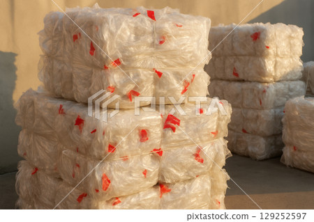 Large stacks of compressed transparent plastic film bales prepared for recycling at an industrial facility under natural sunlight, AI Generative 129252597