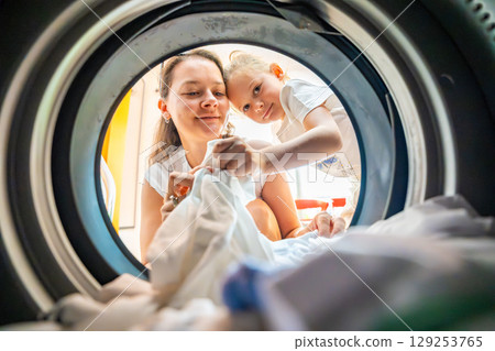 Mother and daughter doing laundry together in a self-service public laundromat, sharing household chores, building responsibility and cooperation in everyday family routine Mother and daughter doing laundry together in a self-service public laundromat, sharing household chores, building responsibility and cooperation in everyday family routine 129253765