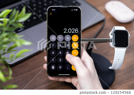 Human hand using a smartphone calculator displaying 2.026 for financial management on a modern office desk with technology 129254568