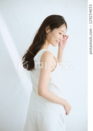 Smiling young woman touching her skin and doing skin care - Smiling young woman touching her skin and doing skin care - 129254653