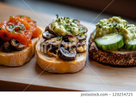 Varied toppings on toasted bread include fresh mushrooms, cucumbers, tomato sauce, and herbs, arranged beautifully on a plate in a bright and inviting kitchen 129254725
