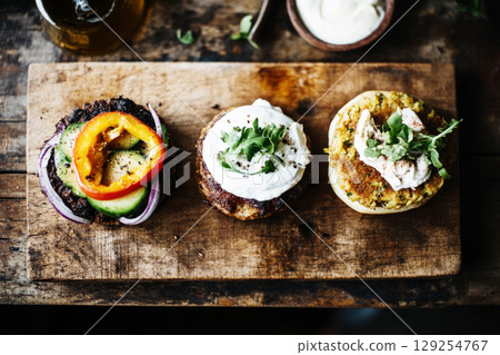 Brightly colored veggie burgers topped with fresh vegetables and sauces sit on a rustic wooden table alongside crispy snacks. A cozy breakfast spread for a flavorful start to the day 129254767