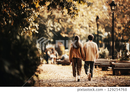 A couple strolls through a beautiful park in autumn, enjoying the fall colors and crisp air. Sunlight filters through the trees, creating a warm, inviting atmosphere 129254768