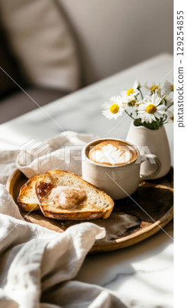 A warm cup of coffee sits beside slices of bread and jam on a wooden tray, complemented by fresh flowers, creating a peaceful breakfast setting perfect for lazy mornings 129254855