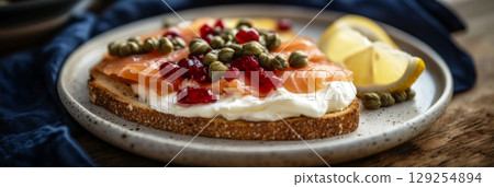 Sliced artisan bread topped with creamy cheese, smoked salmon, tart pomegranate seeds, and capers, served with lemon wedges on a wooden table Sliced artisan bread topped with creamy cheese, smoked salmon, tart pomegranate seeds, and capers, served with lemon wedges on a wooden table 129254894