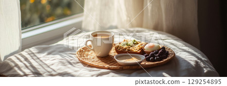 Enjoy a relaxing morning with a delightful breakfast spread on a bed featuring eggs cooked to perfection, toast, fresh salad, and a warm beverage under soft sunlight, banner 129254895