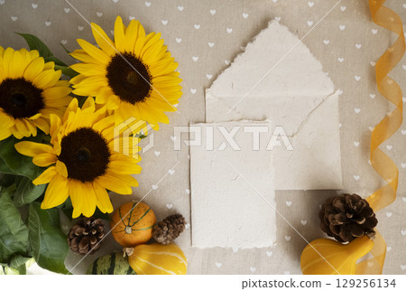 Autumn flatlay with handmade paper card, envelope, sunflowers, mini pumpkins, pine cone, yellow ribbon. Rustic mockup template for greeting or wedding invitation presentation design, selective focus 129256134
