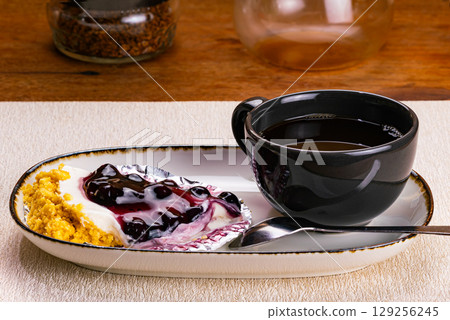 Side view of a cup of coffee in black ceramic cup with blueberry cheese pie on foil paper 129256245