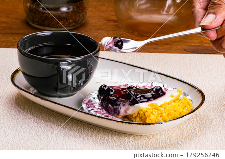Taking a bite of blueberry cheese pie in white ceramic tray with black coffee in black ceramic coffee cup. 129256246
