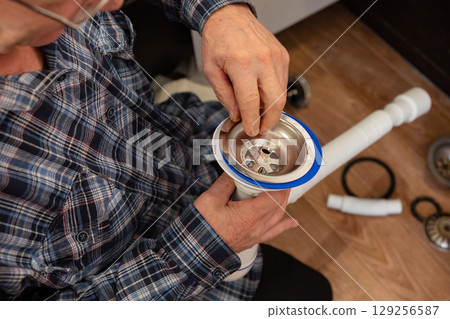 Person assembles plumbing fixtures while sitting on a wooden floor in a home renovation project 129256587