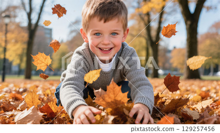Smiling little boy playing with autumn leaves in park on sunny day. Joyful childhood moment during fall season outdoors. 129257456