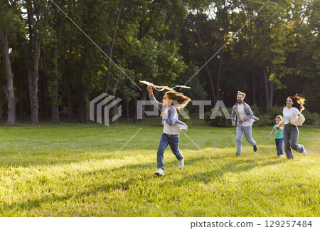 Happy family flying kite in summer park, parents and kids running, playing together outdoors Happy family flying kite in summer park, parents and kids running, playing together outdoors 129257484