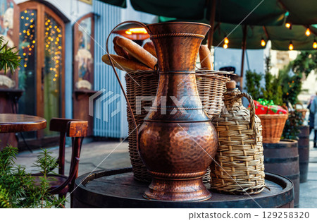 Vintage copper jug braided wine bottle and baguette on wooden barrel 129258320