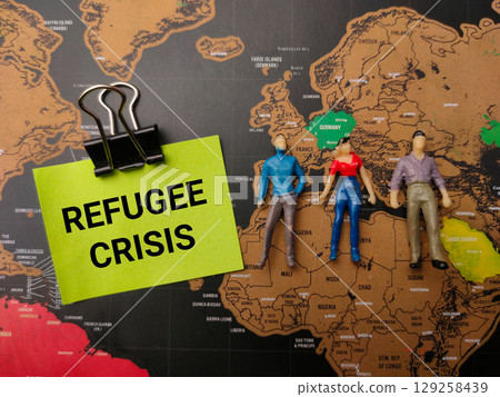 Miniature people and sticky note with the word REFUGEE CRISIS on a world map background. 129258439