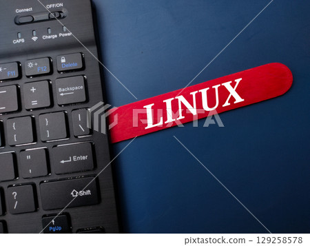 Black keyboard and ice cream stick with the word LINUX on a blue background. Black keyboard and ice cream stick with the word LINUX on a blue background. 129258578